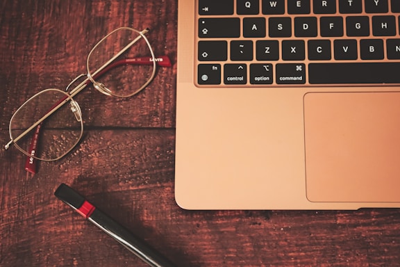 a pair of glasses sitting on top of a wooden table next to a laptop computer