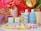 A colorful arrangement featuring skincare products, including bottles labeled 'function of beauty' for shampoo and conditioner. Small boxes for haircare booster shots are also present. The scene is accentuated with vibrant flowers in vases and pastel-colored pom-poms scattered around.