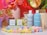 A colorful arrangement featuring skincare products, including bottles labeled 'function of beauty' for shampoo and conditioner. Small boxes for haircare booster shots are also present. The scene is accentuated with vibrant flowers in vases and pastel-colored pom-poms scattered around.