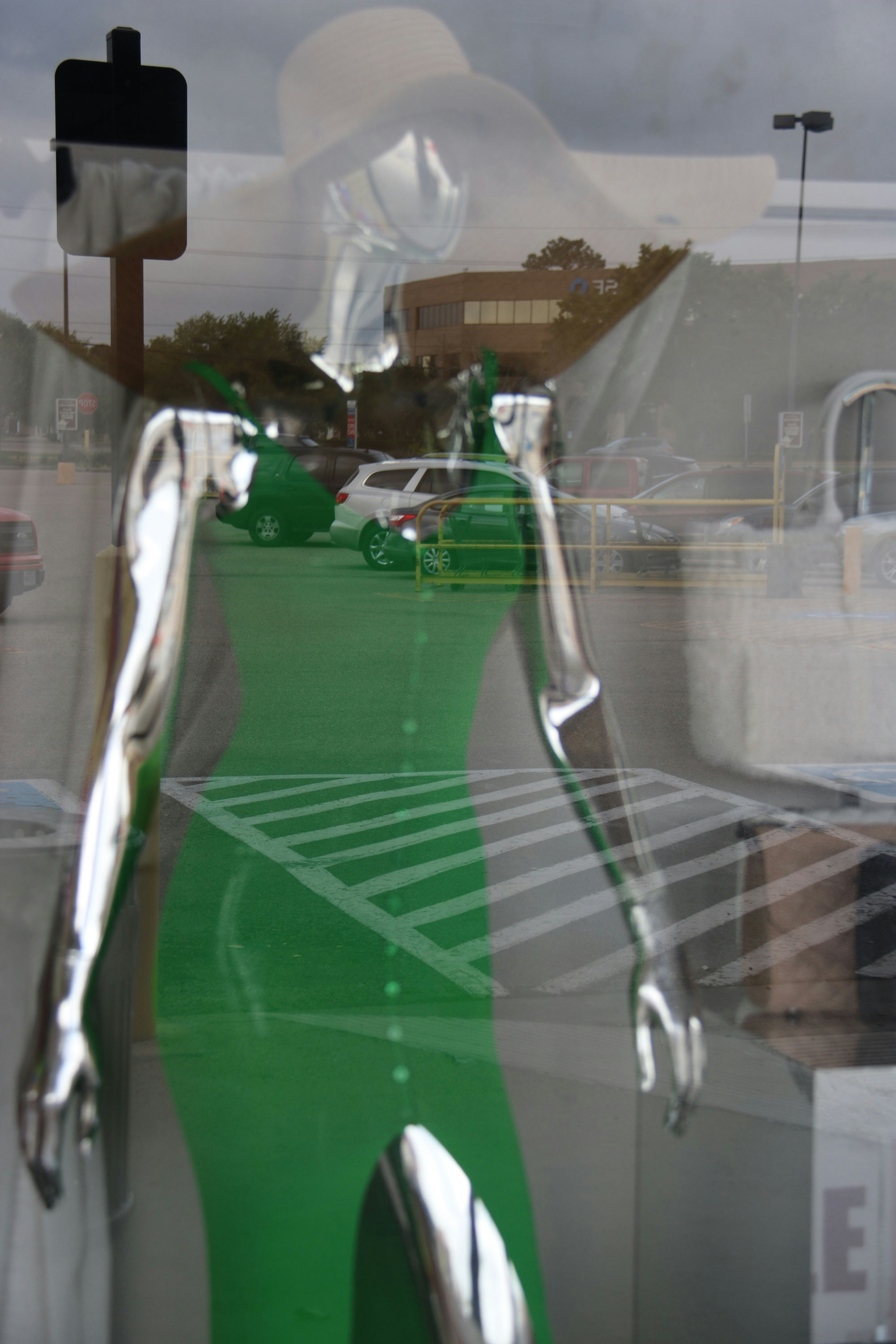 a mannequin in a green dress is reflected in a window