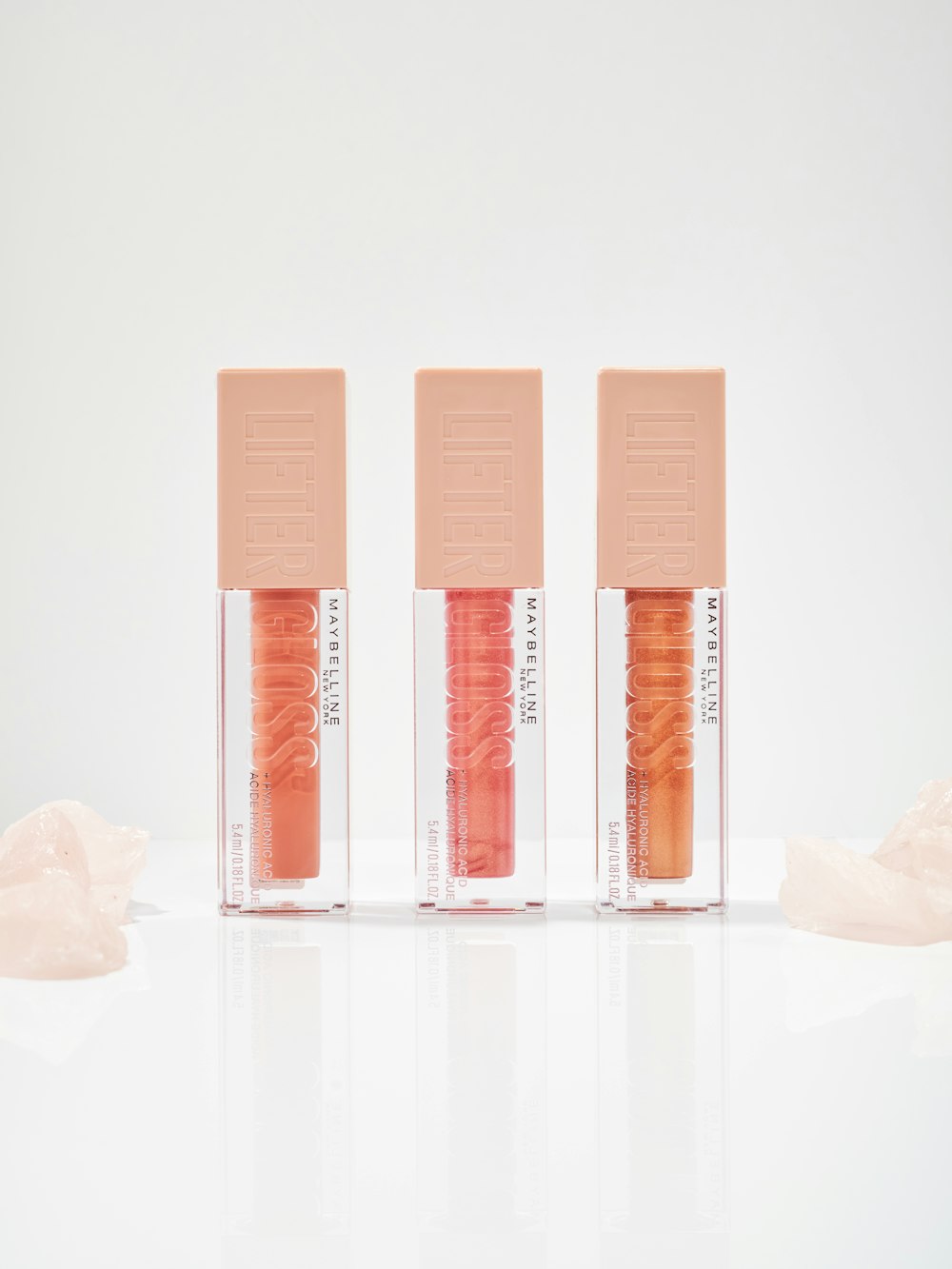 three lip glosses in a row on a white surface