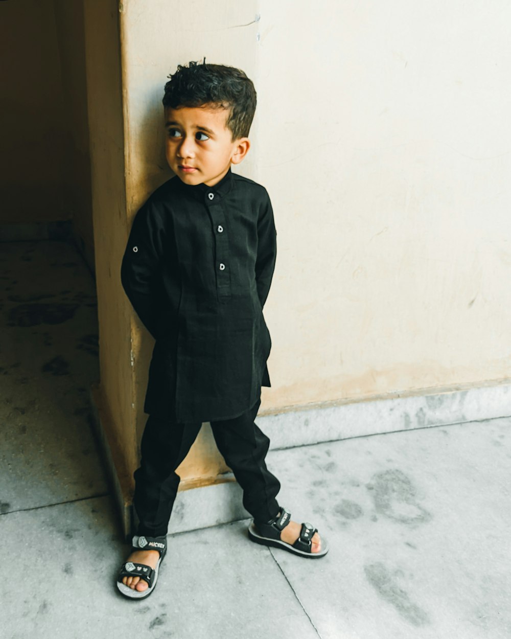 a little boy standing next to a wall
