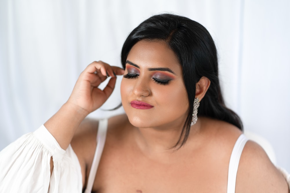 a woman in a white top is putting on makeup