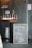 A row of beer bottles with colorful labels is placed on a wooden table beside a chalkboard sign reading 'Welcome to Stave & Nail Brewing Co.' A metal beer keg is positioned nearby, and several beer taps are affixed to a grey wall.