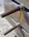 Two large metal bolts with nuts are fastened onto a metal surface, exhibiting visible rust on one of the bolts. The background features pebbled ground with soft focus.