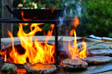 Close-up of sizzling carne asada on a hot grill with flames flickering.