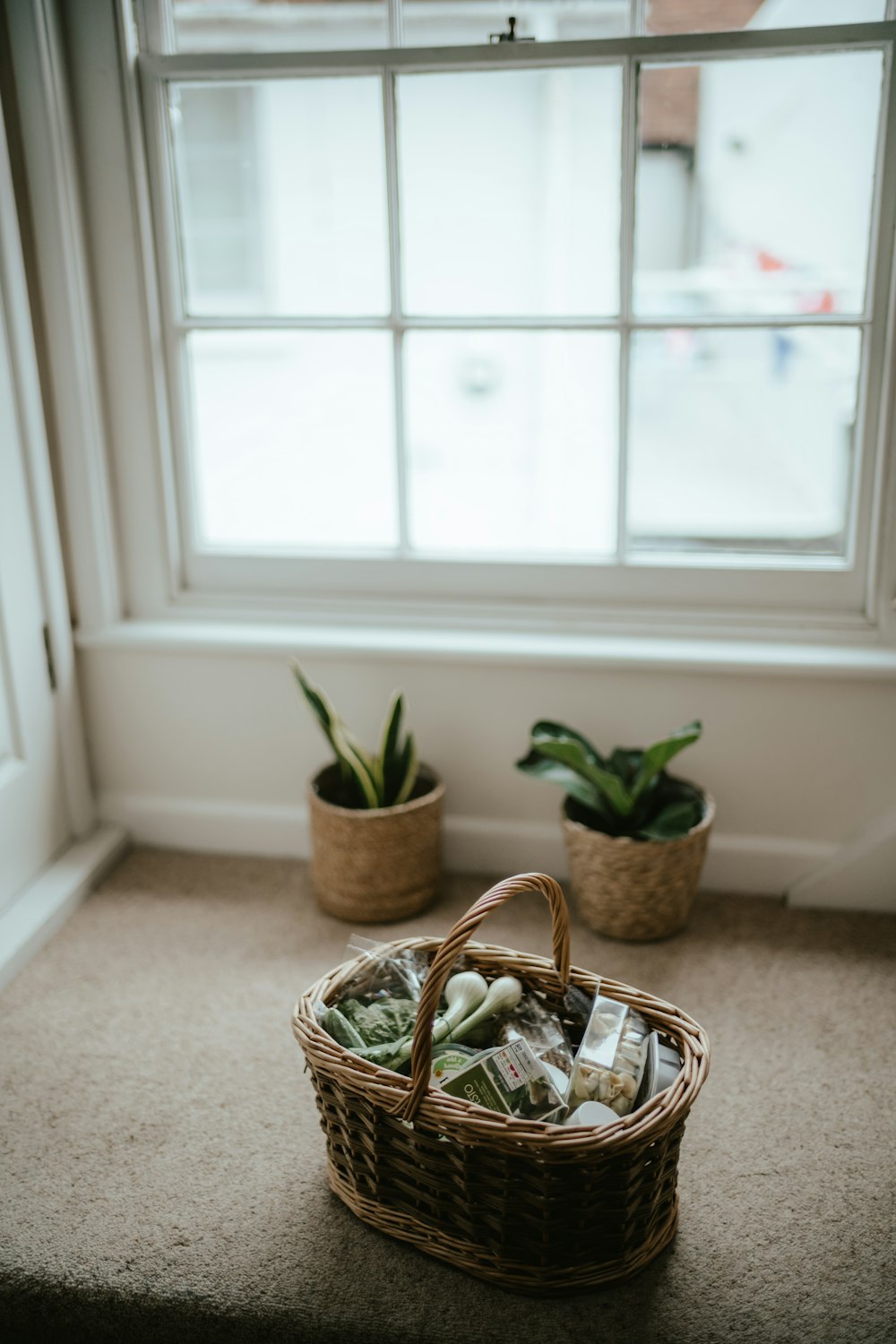 a wicker basket filled with rocks and plants next to a window