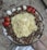 A large metal platter filled with a mix of cooked brown beans and topped with a large, folded yellow omelette. Surrounding the beans are several pieces of sliced red and white onions, as well as halved red bell peppers. The platter is placed on a marbled surface.
