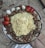 A large metal platter filled with a mix of cooked brown beans and topped with a large, folded yellow omelette. Surrounding the beans are several pieces of sliced red and white onions, as well as halved red bell peppers. The platter is placed on a marbled surface.