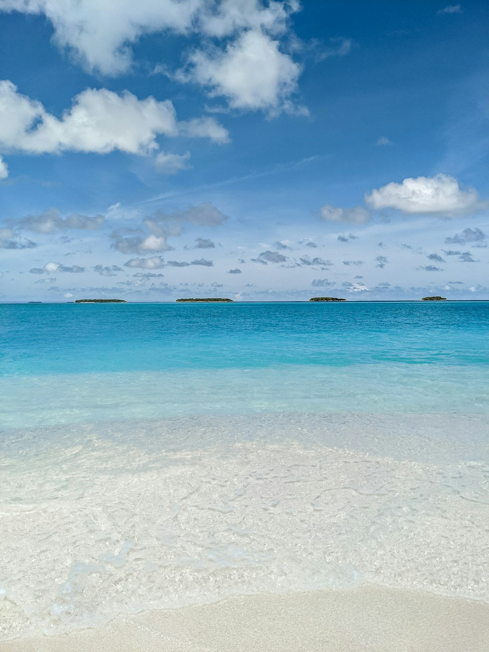 a sandy beach with blue water and clouds