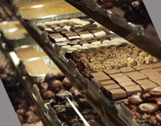 A display case filled with a variety of chocolates and confections, arranged in neat rows on trays. Different types of chocolates, including ones with nuts and cream fillings, can be seen.