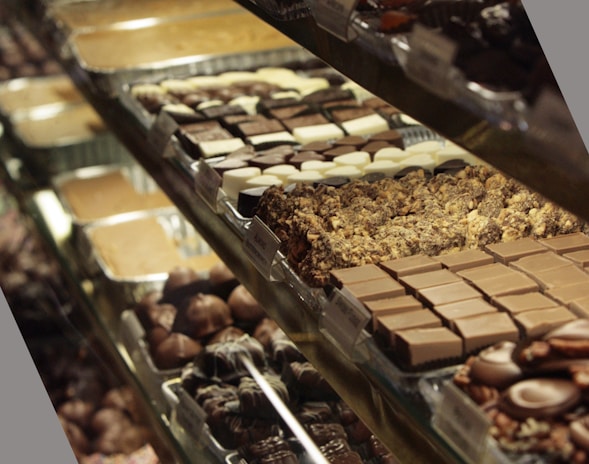 A display case filled with a variety of chocolates and confections, arranged in neat rows on trays. Different types of chocolates, including ones with nuts and cream fillings, can be seen.