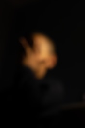 A blurry and indistinct image with what appears to be a person covering their face against a dark background.