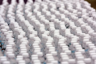 Rows of identical plastic water bottles are closely arranged, creating a pattern of white caps against clear bottles. The bottles are tightly packed, emphasizing uniformity and mass production.