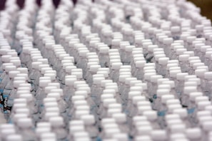 Rows of identical plastic water bottles are closely arranged, creating a pattern of white caps against clear bottles. The bottles are tightly packed, emphasizing uniformity and mass production.