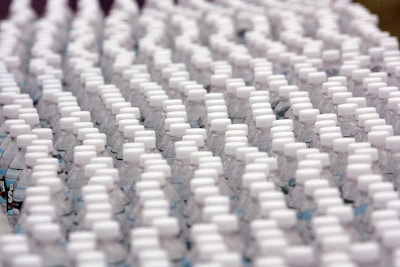 Rows of identical plastic water bottles are closely arranged, creating a pattern of white caps against clear bottles. The bottles are tightly packed, emphasizing uniformity and mass production.