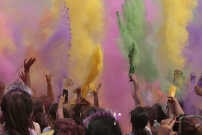 Children and adults laughing together while throwing vibrant yellow and green powder in the air.
