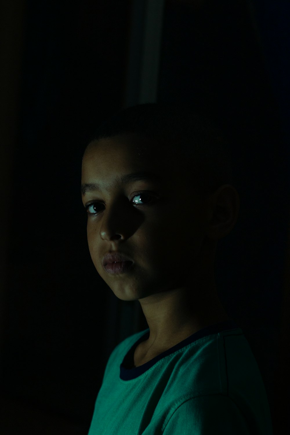 a young boy in a dark room looking at the camera