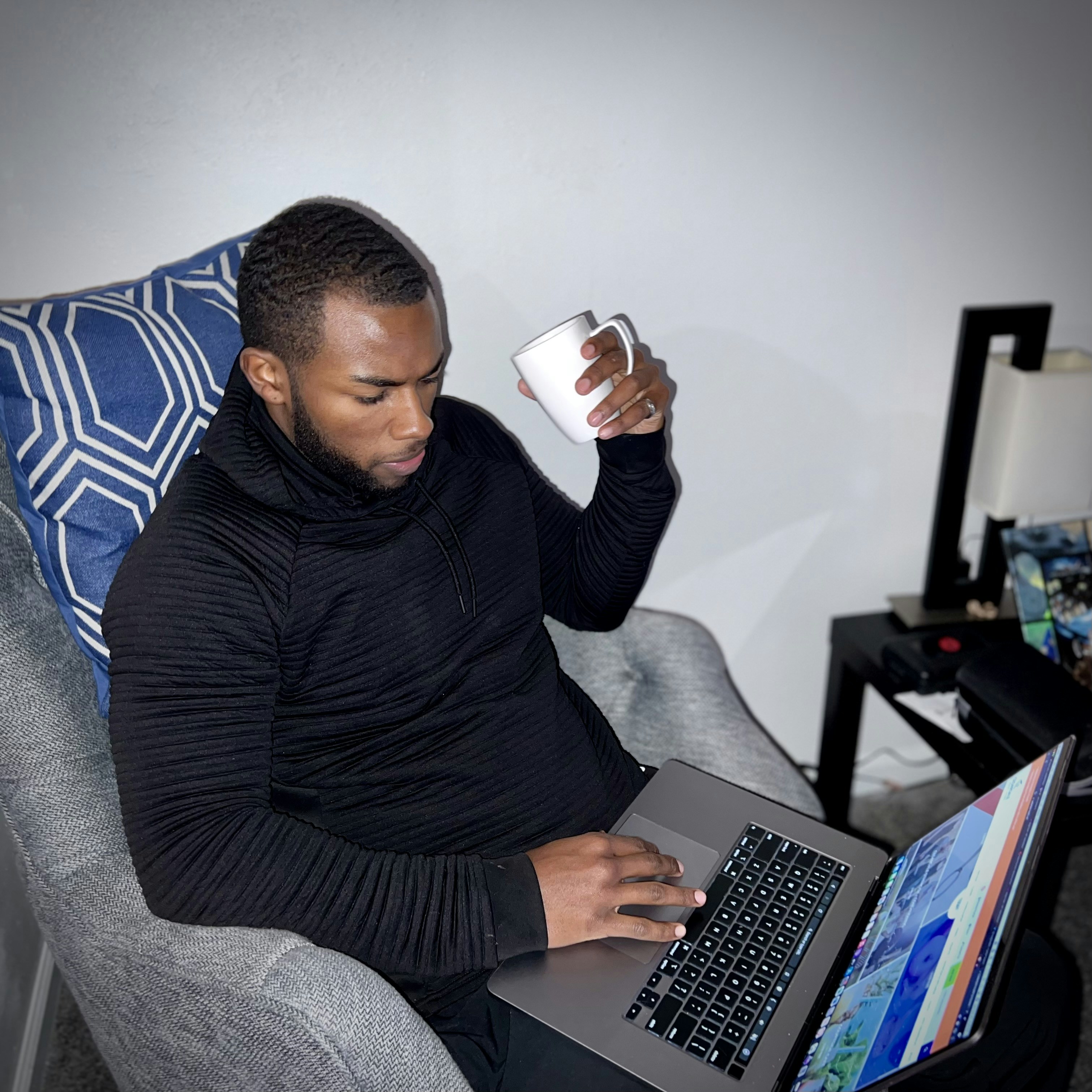 Seorang pria duduk di kursi dengan laptop dan secangkir kopi