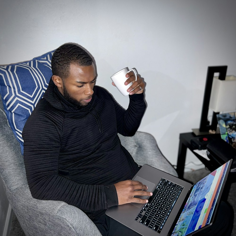 a man sitting in a chair with a laptop and a cup of coffee