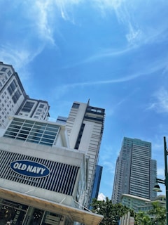 Several modern high-rise buildings against a clear blue sky, with a prominent Old Navy storefront in the foreground. The scene conveys a bustling urban environment with an emphasis on modern architecture.