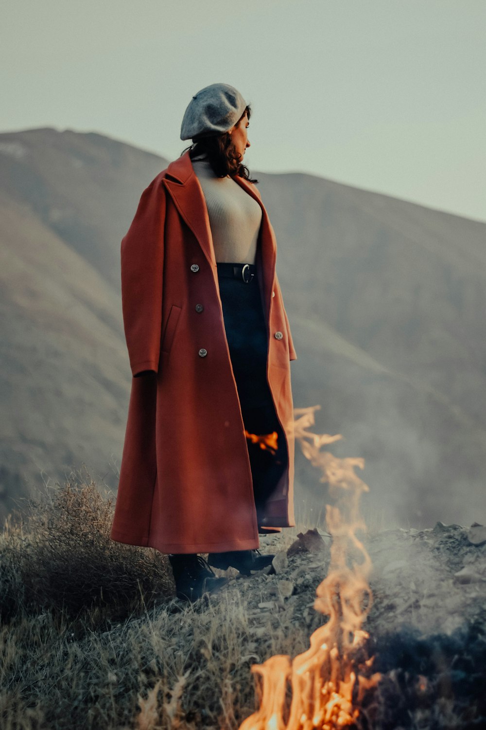 a woman in a red coat standing in front of a fire