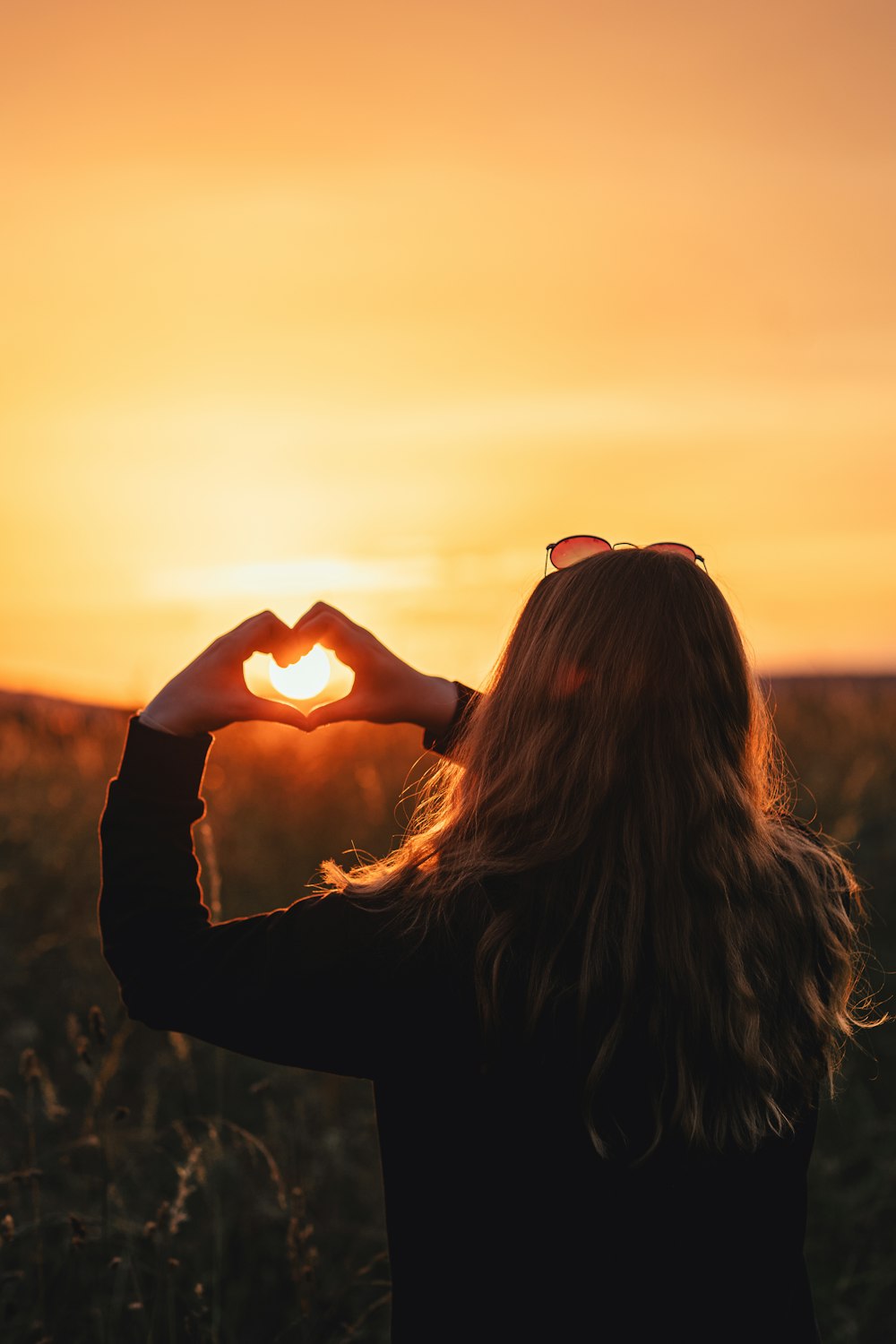 a woman standing in a field with her hands in the shape of a heart