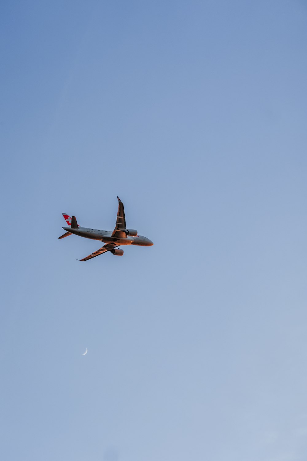 an airplane flying in the sky with a half moon in the background