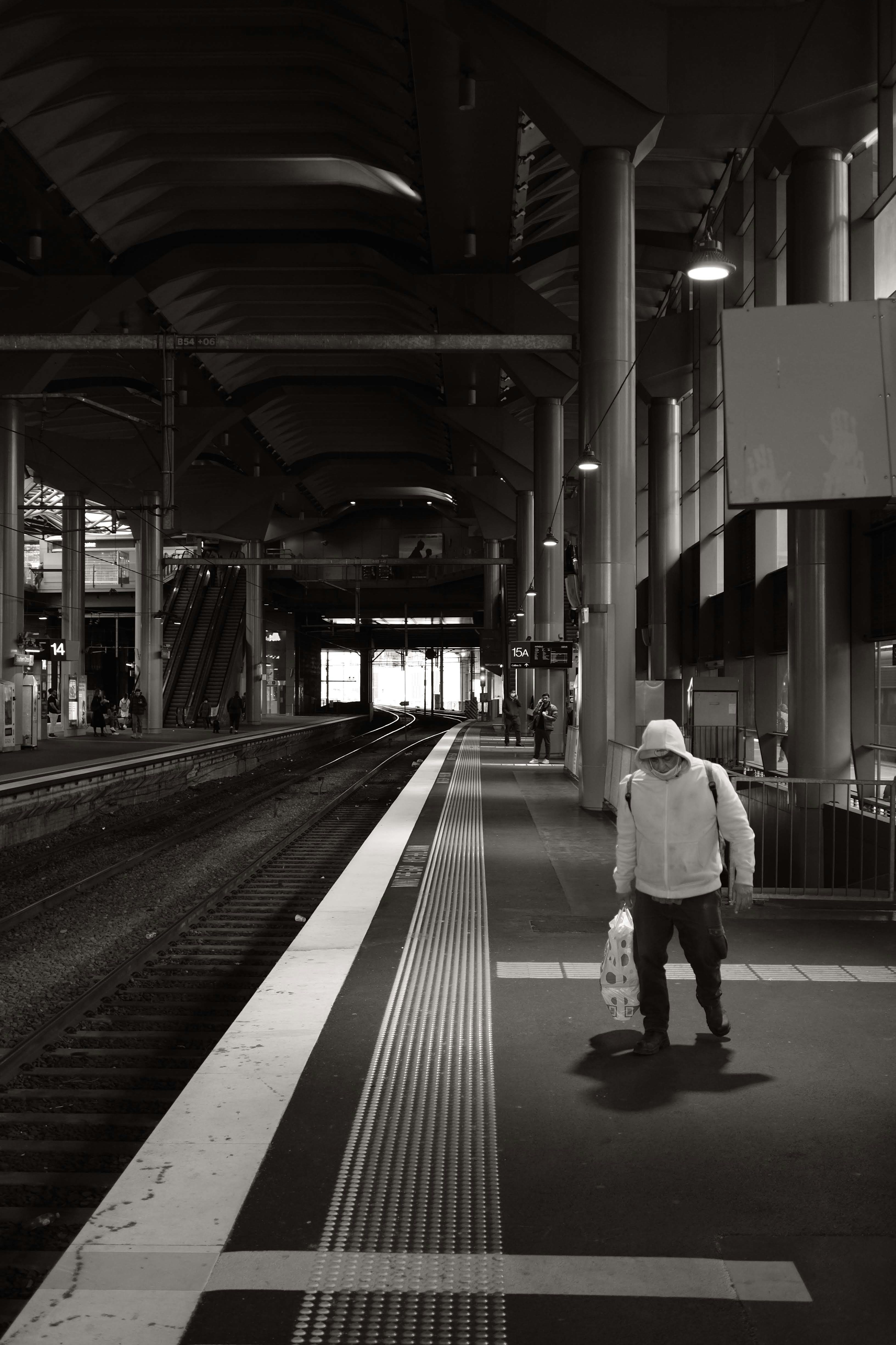 A commuter wearing a large warm jacket walks under a streetlight on the train platform