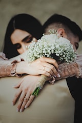 Close-up of hands holding flower bouquets and wedding rings, symbolizing love.