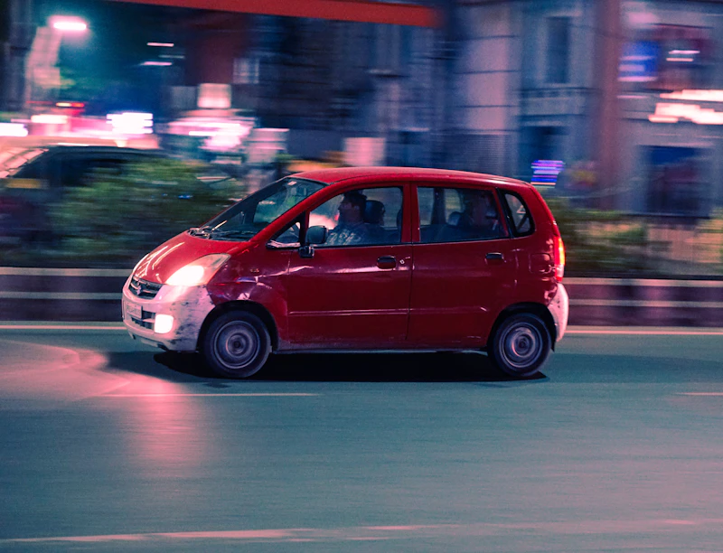 Small red car driving down a city street