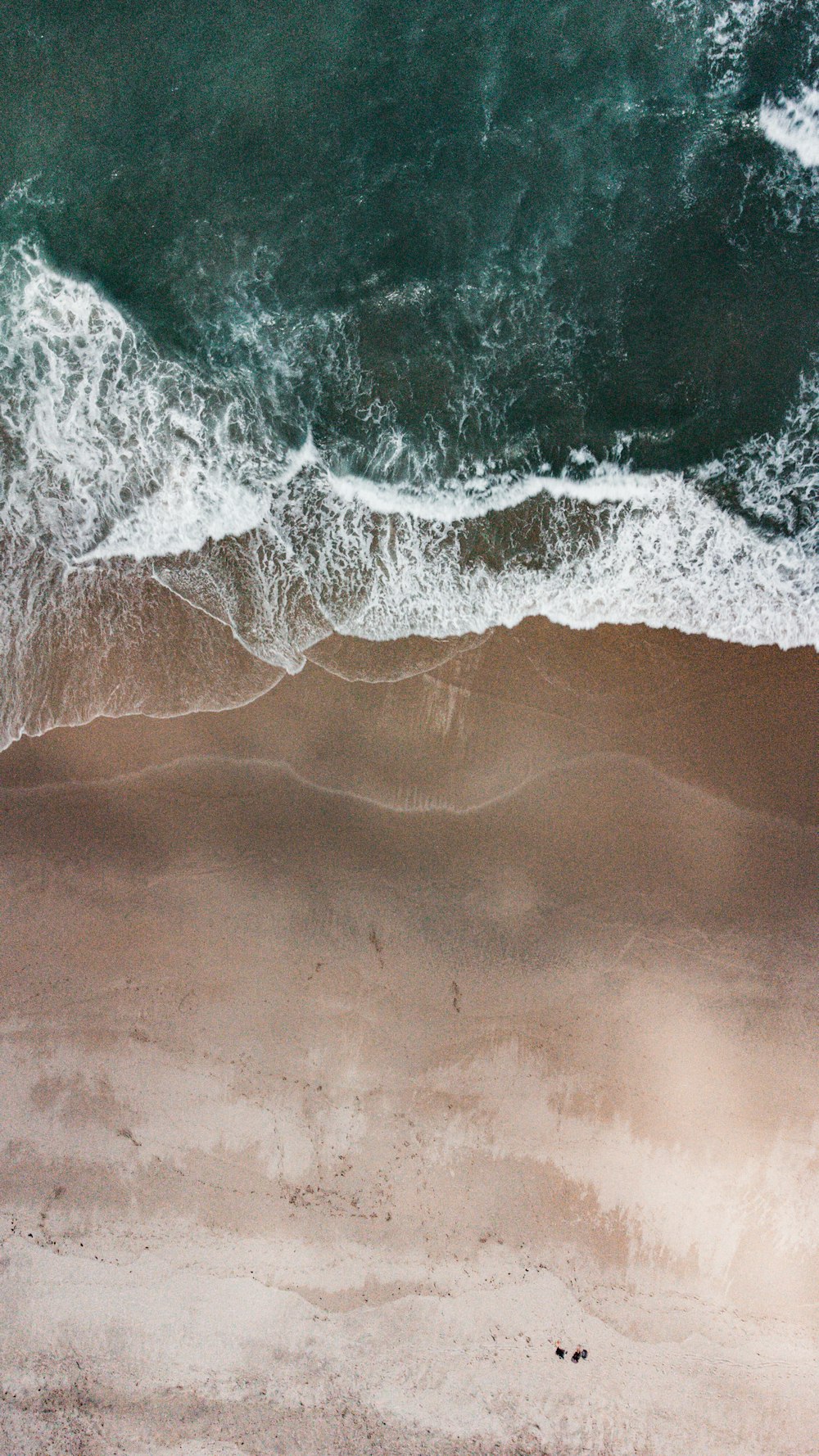 an aerial view of a sandy beach with waves