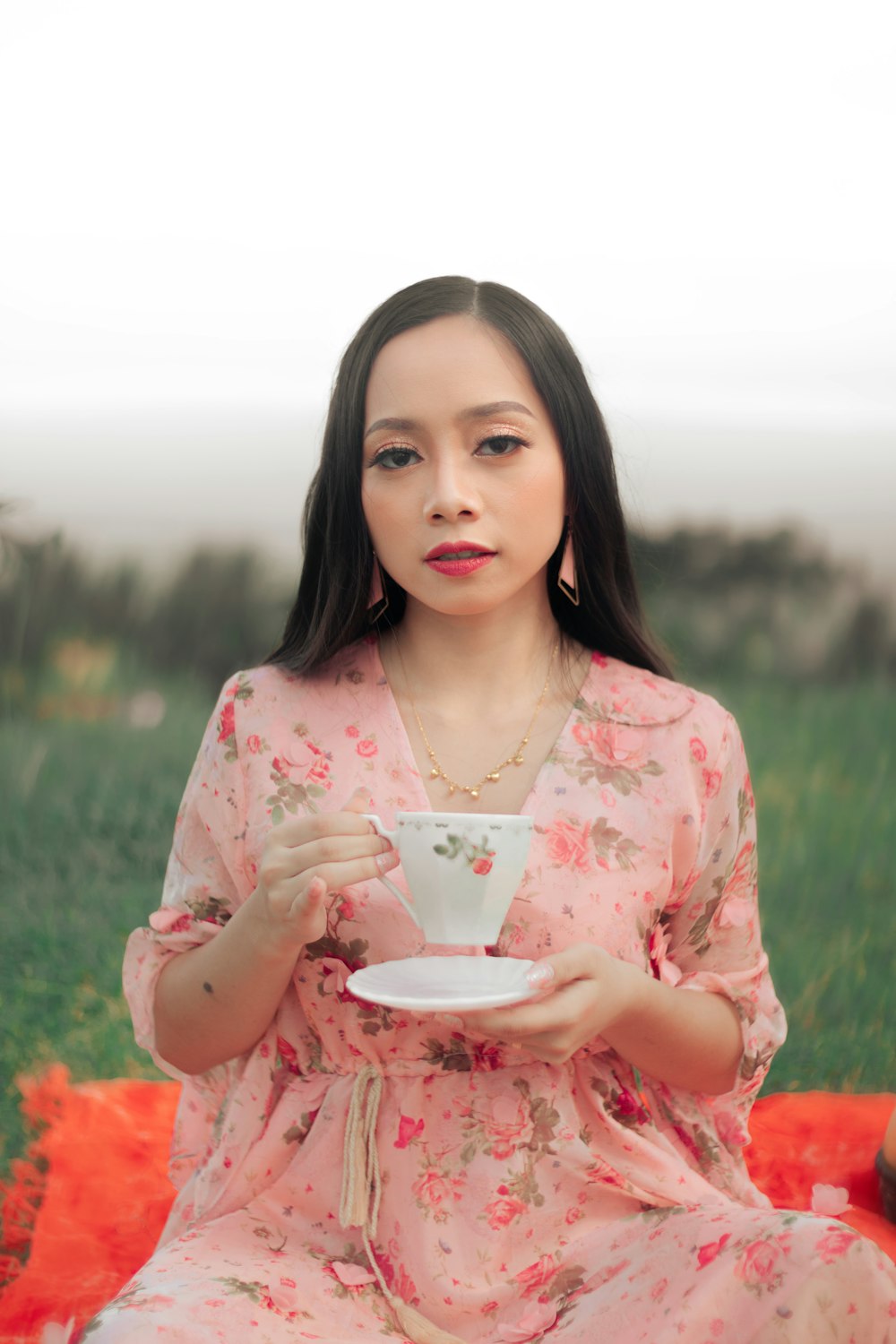 a woman sitting on a blanket holding a cup