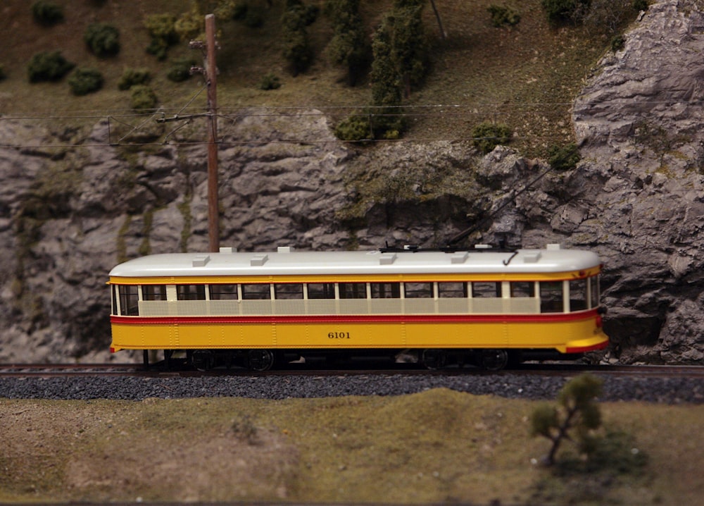 a yellow and red train traveling past a rocky cliff