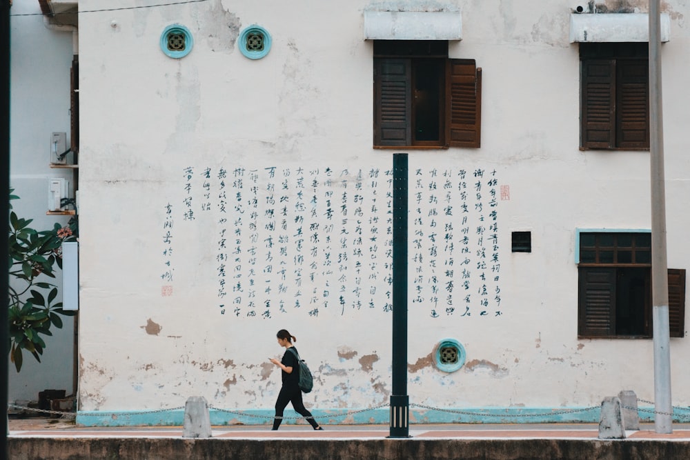 a woman walking down a street past a white building