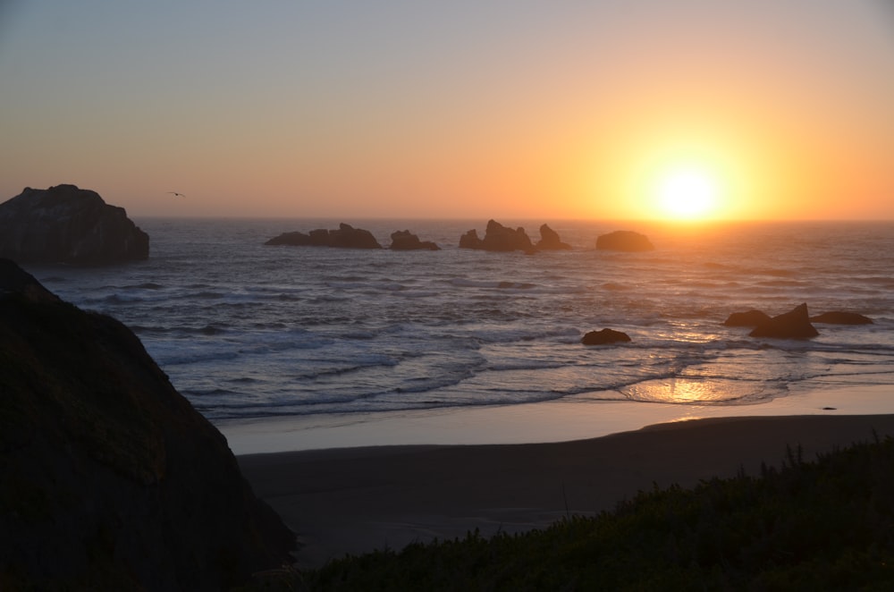 the sun is setting over the ocean and rocks