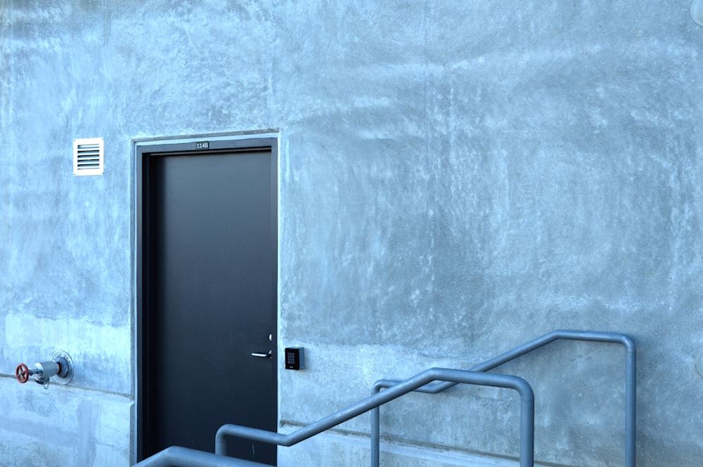 a door and a hand rail in front of a concrete wall