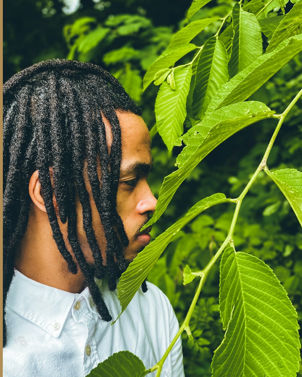 a man with dreadlocks standing in front of a tree