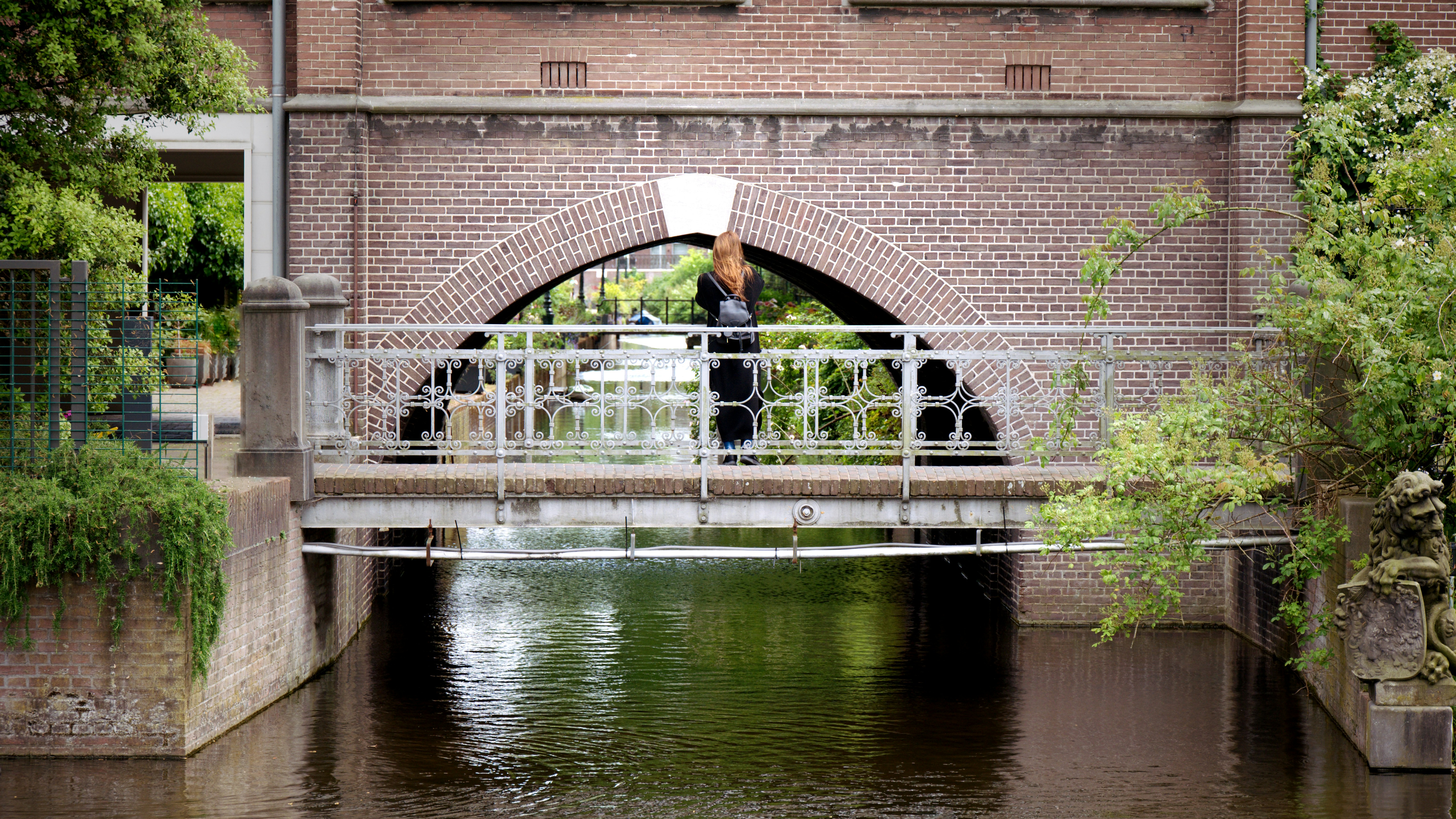 a man standing on a bridge over a river, A girl taking a picture of the canal under the bridge. 