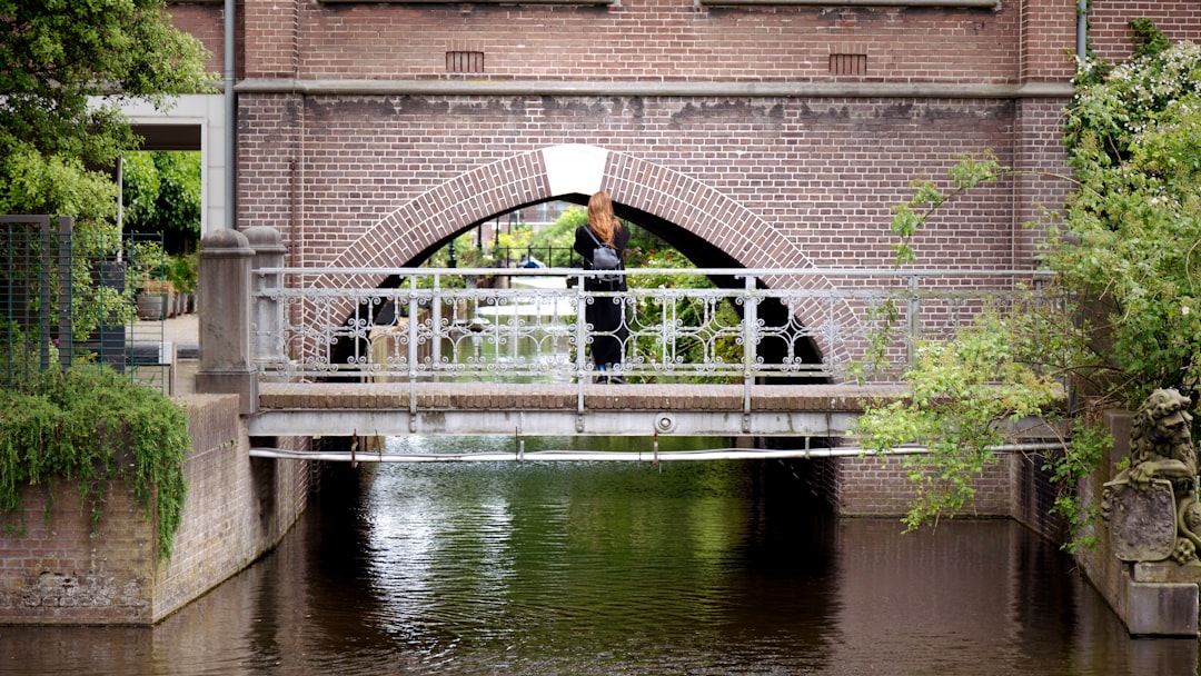 a man standing on a bridge over a river, A girl taking a picture of the canal under the bridge.