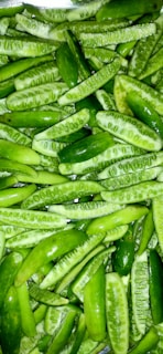 A pile of green mini cucumbers that have been cut in half lengthwise. The cucumbers are fresh, with visible seeds and a shiny surface.