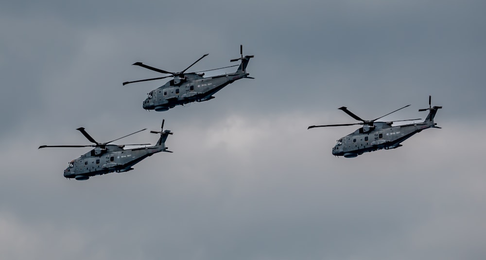 three military helicopters flying in formation in a cloudy sky