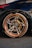 A close-up of a car's wheel featuring a high-performance tire with the brand name 'Hankook' visible. The wheel has a sleek, modern design with a metallic finish and copper-colored rim. The brake caliper is visible inside, adding to the sporty aesthetic. The car's body is dark and glossy, reflecting the surroundings.