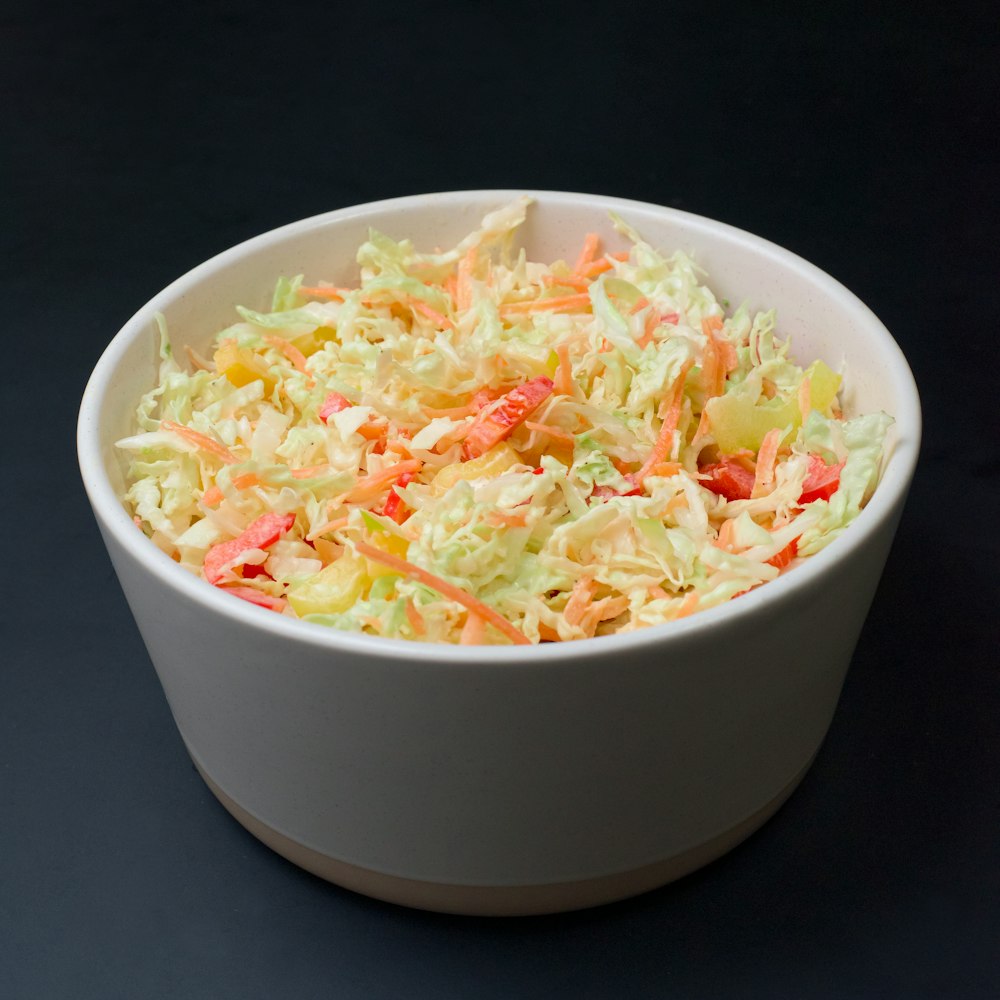 uma tigela branca cheia de coleslaw em cima de uma mesa