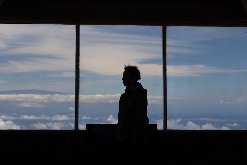 a man standing in front of a window looking out at the clouds
