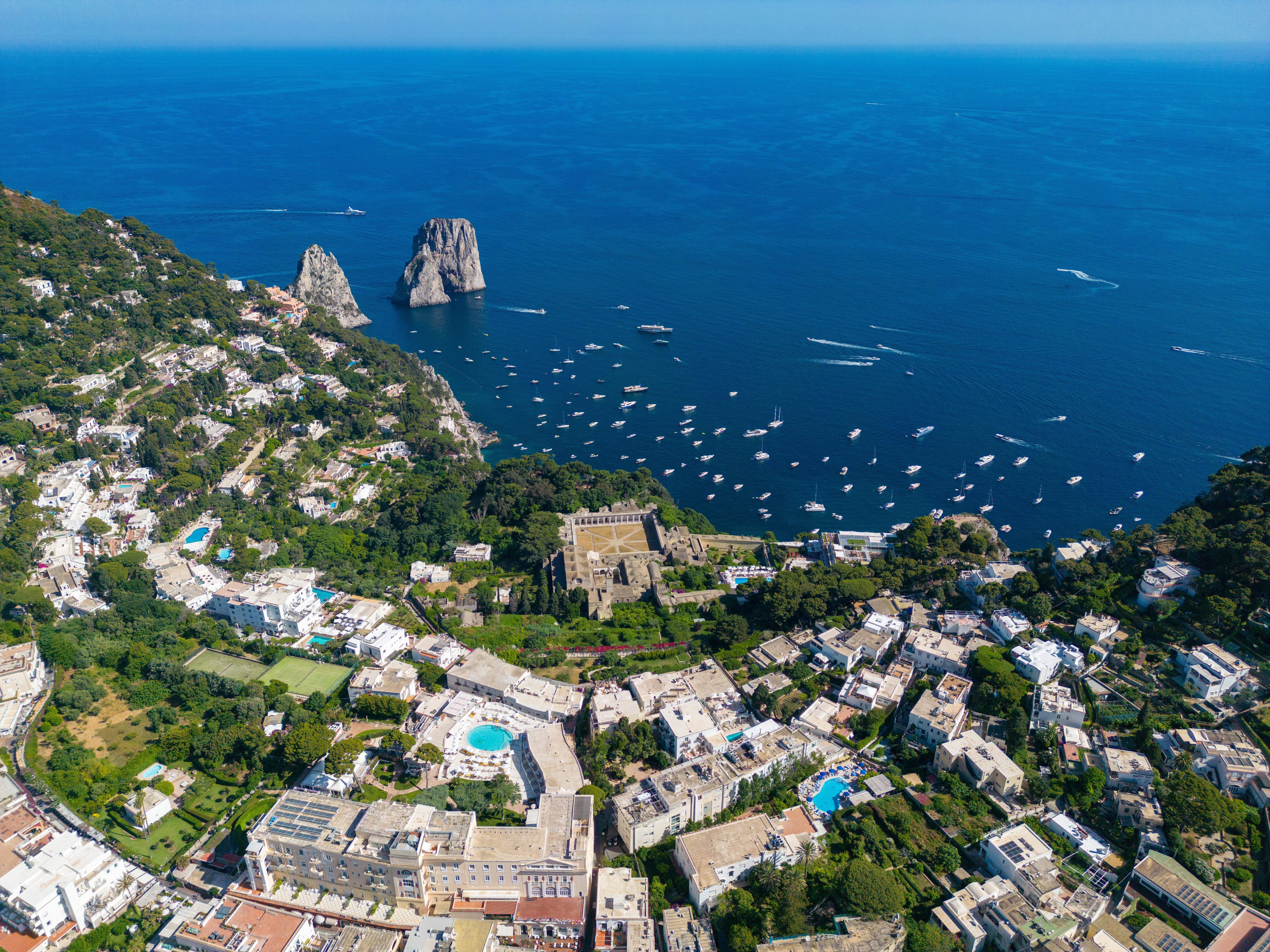 Aerial drone view of Capri island, Italy — turquoise waters, white buildings, and the harbour of Marina Grande seen from above, the setting for Dickie Greenleaf's villa in Netflix's Ripley