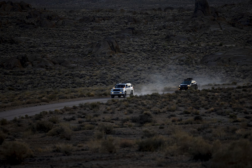 two trucks driving down a dirt road in the desert