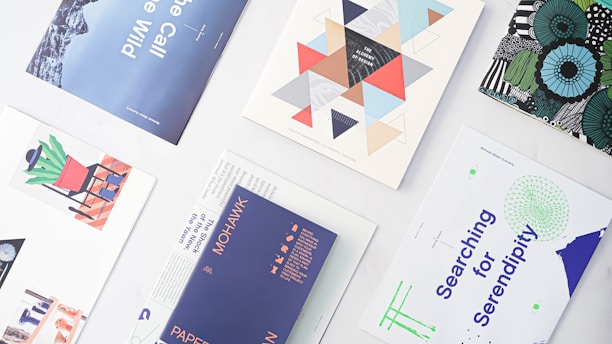 A collection of various prints and posters arranged on a white surface, featuring diverse designs and color schemes. The designs include geometric shapes, modern art illustrations, abstract patterns, and text-based artwork. The prints vary in themes and colors, showcasing creativity and graphic design diversity.