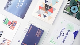 A collection of various prints and posters arranged on a white surface, featuring diverse designs and color schemes. The designs include geometric shapes, modern art illustrations, abstract patterns, and text-based artwork. The prints vary in themes and colors, showcasing creativity and graphic design diversity.