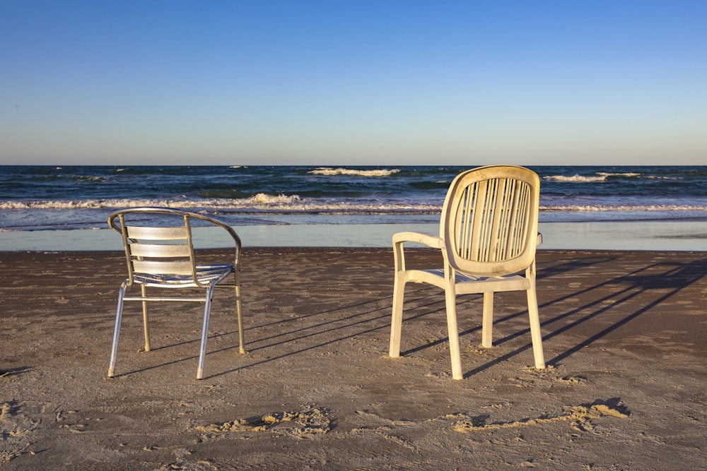 a couple of chairs sitting on top of a sandy beach